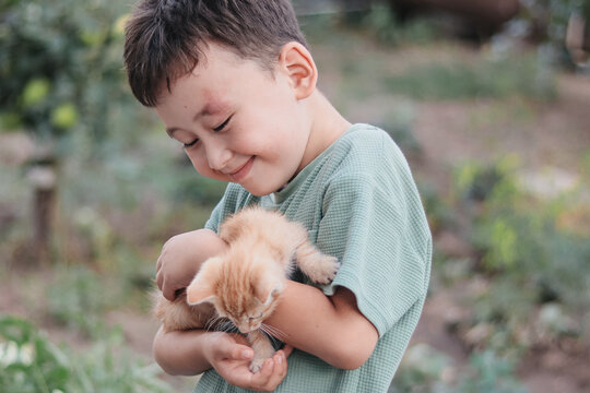 Boy holding kitten in green garden with copy space. Concept of care, responsibility, childhood bonding, pet ownership.