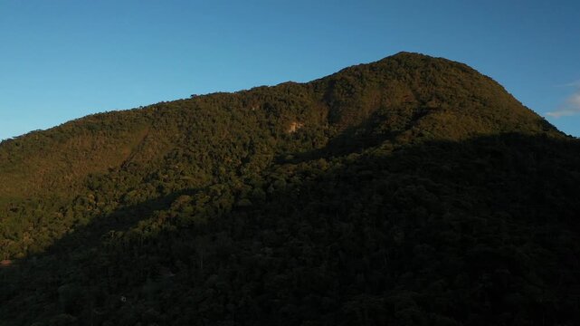Aerial view of a dense tropical mountain forest at sunset with deep shadows and golden light on the canopy