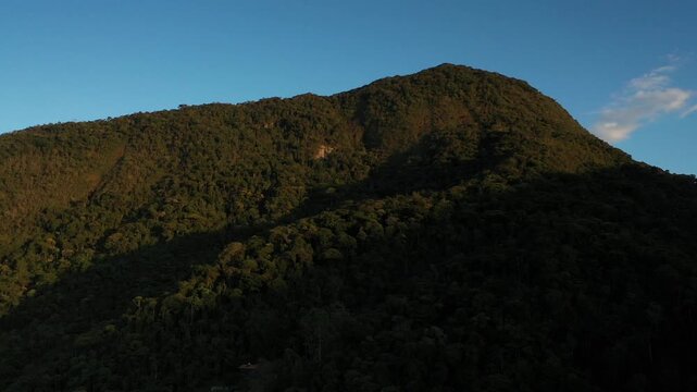 Aerial view of a dense tropical mountain forest at sunset with deep shadows and golden light on the canopy