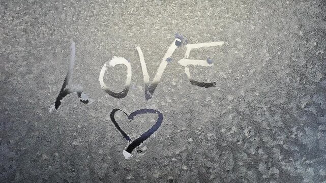handwritten text love and heart shape on frosty car window melting