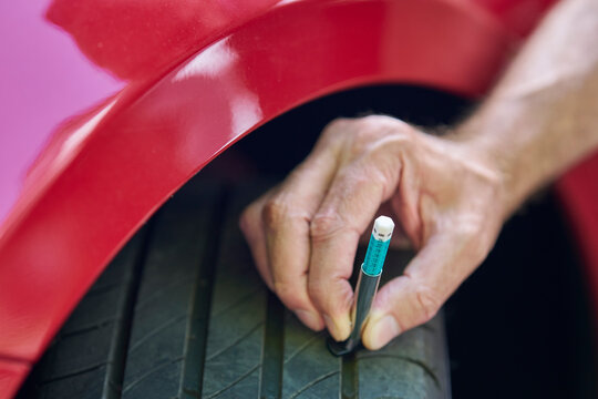 Close up of man using  gauge to check tyre tread depth on car