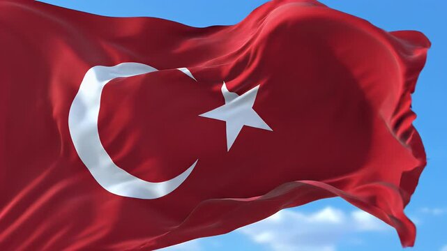 A close-up of a red flag with a white crescent moon and star against a blue sky