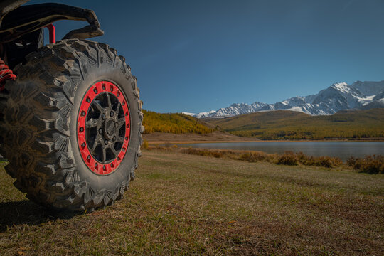 Close up of UTV off-road vehicle wheel with red beadlock on a mountain meadow by a lake. Expedition, extreme adventure travel and overlanding concept in autumn.