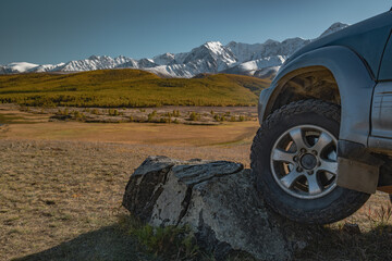 Fototapeta premium Close up of off-road 4x4 vehicle wheel climbing a large rock in a mountain valley against snow peaks. Suspension articulation, expedition and adventure travel concept.