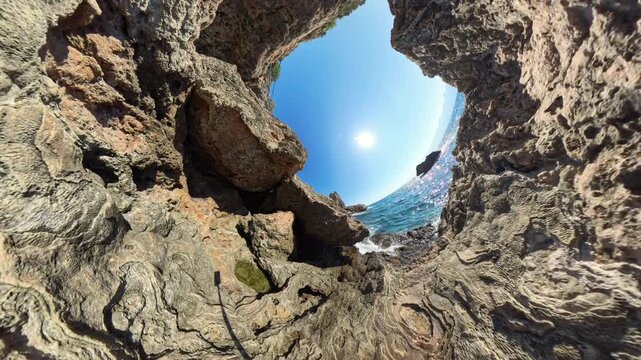 360 degree camera. A view from between two rocky cliffs looking up toward the sun. The sunlight reflects off the rugged terrain, illuminating the natural landscape. A wide-angle shot of the scene.