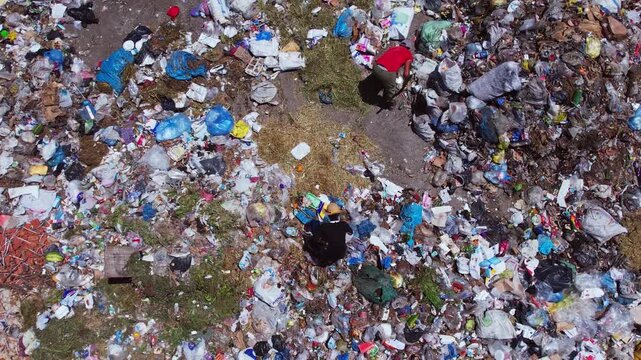 Aerial view of people collecting waste in a landfill with dense garbage accumulation. Scene highlights environmental pollution, waste management, recycling, and human labor.