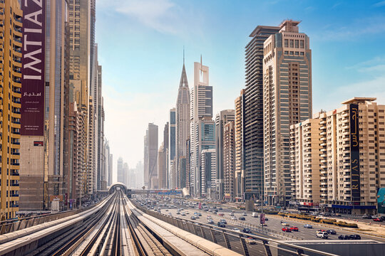 10 January 2025, Dubai, UAE: cityscape featuring a modern metro railway track parallel to a busy highway, surrounded by towering skyscrapers