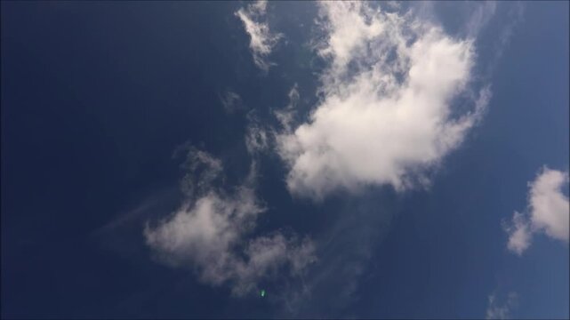 Bright white clouds drift across a deep blue sky on a sunny day