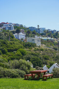 South Africa,Mossel Bay,Bartolomeu Dias Museum Complex,Picnic table in a grassy park overlooking a hillside residential area with houses and greenery under a clear blue sky