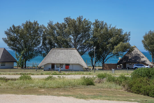 South Africa,Garden Route,Traditional thatched-roof houses near a coastal area with trees and clear blue sky