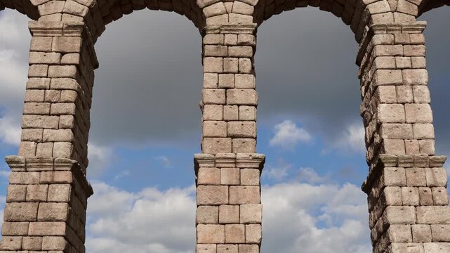 View of the Roman aqueduct in Segovia, Spain, featuring iconic stone arches against a blue sky with clouds, showcasing ancient engineering and historic architecture.
