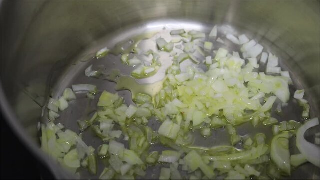 Chopped onions sizzling in olive oil in a stainless steel pot