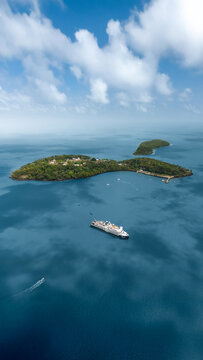 Aerial view of the Iles du Salut archipelago with a cruise ship anchored in turquoise waters under a cloudy sky in Iles du Salut, French Guiana.