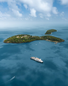 Aerial view of the lush green Salvation Islands surrounded by turquoise ocean waters with a large cruise ship anchored nearby in Iles du salut, French Guyana.
