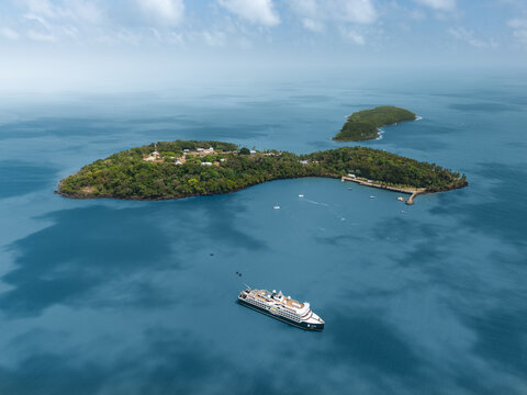 Aerial view of the lush green Iles du Salut archipelago with a large cruise ship anchored in the deep blue Atlantic waters near Iles du Salut, French Guiana.