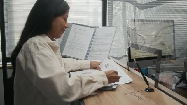 Medium side shot of young Hispanic woman listening to advice from helpful Caucasian female American consulate officer on completing application form, while submitting documents for USA tourist visa