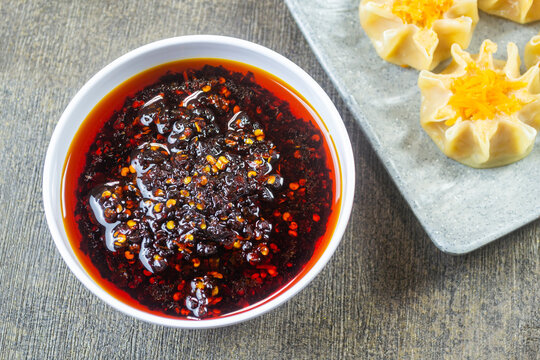 Spicy Chinese chili oil in a white bowl with steamed chicken dimsum shumai siomay in the background