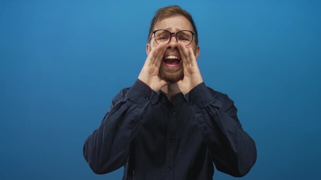 Man cupping hands and shouting with open mouth in studio against blue backdrop; enthusiasm communication.