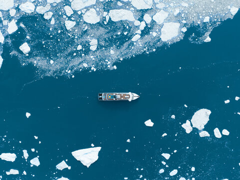 Aerial view of a cruise ship navigating through deep blue water and scattered white icebergs Greenland.