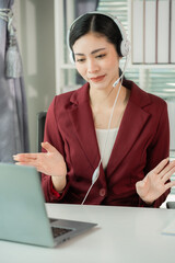 The photograph shows an Asian businesswoman using a laptop and headphones in an office, chatting online while using the laptop.