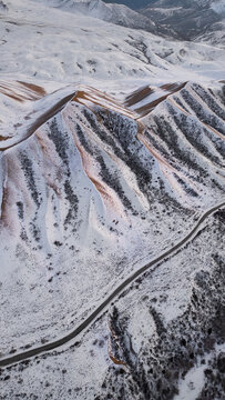 Aerial view of snow-covered mountain ridges and a winding road through the rugged winter landscape in Kazakhstan.
