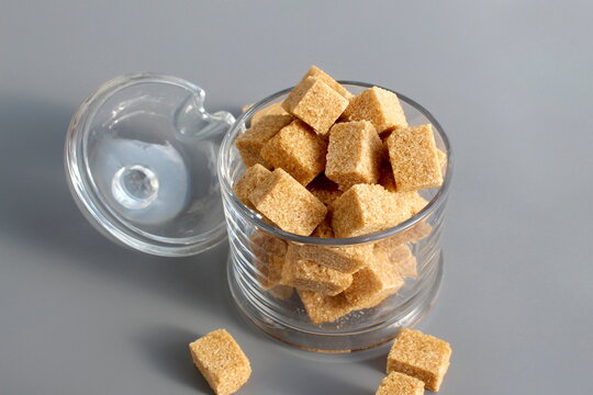 A glass bowl with brown lump sugar stands on a grey background.