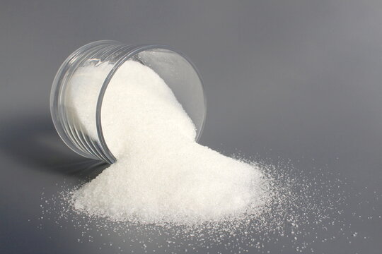 On a grey background lies an overturned sugar bowl with granulated sugar.