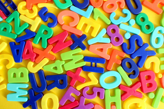 Abstract texture of many bright multi-colored letters lying on a yellow background.