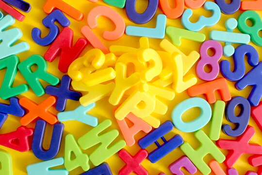 A pile of multi-colored letters of the English alphabet lie on a yellow background.