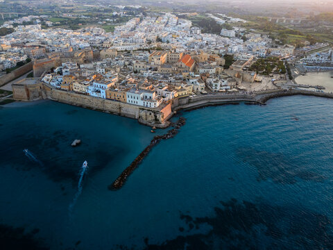 Aerial view of the historic center with white buildings and ancient defensive walls along the turquoise sea in Otranto, Apulia, Italy.