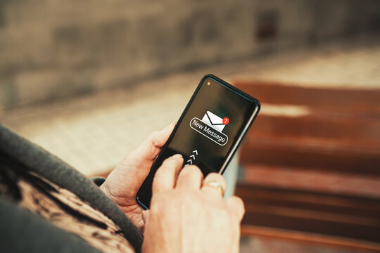Smartphone notification showing new message icon in senior woman's hands outdoors. Senior person holding a mobile phone with a "New Message" notification pop-up on screen.