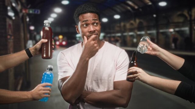 Man weighing multiple bottled drinks while touching his chin with crossed arms on a subway platform inside a station building; hesitation choice options.