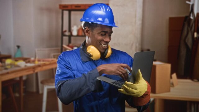 Man construction worker in hardhat holding laptop and gesturing with hand in building; productivity problem solving.