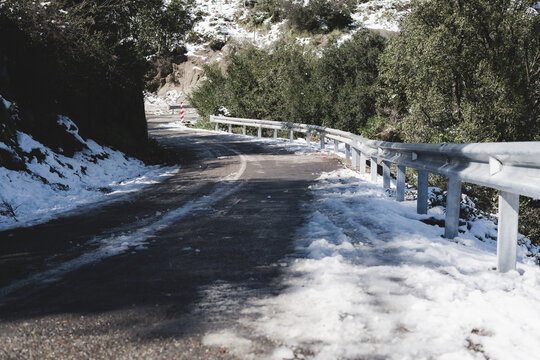 Carretera estrecha de monta&ntilde;a parcialmente cubierta de nieve y hielo, con baranda met&aacute;lica y entorno natural invernal