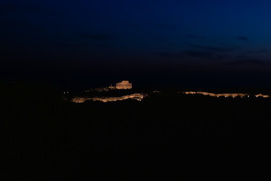 Aerial view of the illuminated Selinunte Archaeological Park with ancient Greek temple columns glowing against the dark night sky in Marinella, Sicilia, Italy.