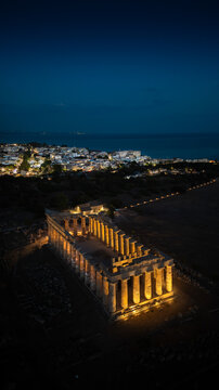 Aerial view of the illuminated Temple of Hera at Selinunte Archaeological Park with the lights of Marinella and the sea at night Marinella, Sicilia, Italy.