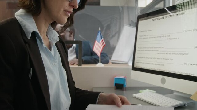 Medium tilting shot of middle-aged Caucasian female American consular officer inspecting visa application, bank statement, employment certificate from senior black man while processing submission
