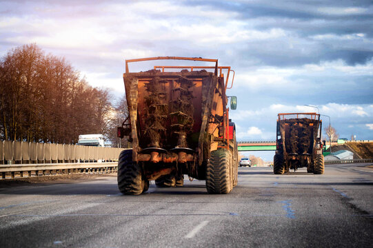 Two heavy agricultural machines laden with organic matter driving on paved road under overcast sky, industrial transportation of cargo. Copy space for text