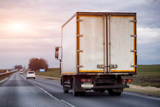 Rear view of cargo truck driving on highway under overcast sky, transportation of goods across landscape, commercial logistics and delivery service, evening sunset. Copy space for text