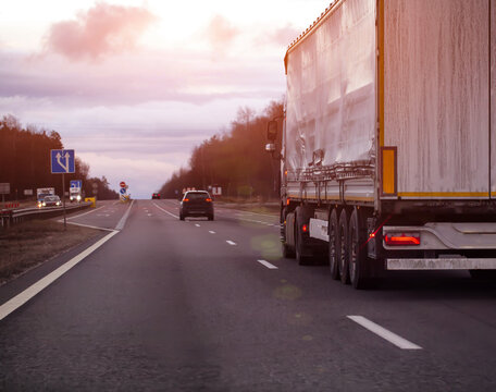 Semi-truck with white trailer traveling on highway at dusk during overcast day, freight transportation along road infrastructure, evening sunset. Copy space for text