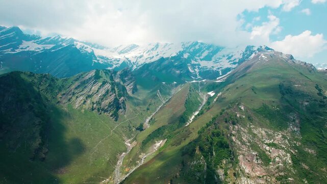 4K aerial view of snow capped Himalayas and river stream flowing through mountain slope as seen from Beas Kund Trek in Himachal Pradesh, India. Summer landscape. Trekking, adventure and travel concept