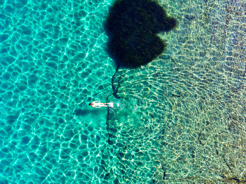 Aerial top-down view of woman snorkelling in crystal clear turquoise water over rocky seabed, Uvala Marculeti, Dalmatian Coast, Croatia