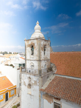 Aerial view of the historic church bell tower with a clock and weathered white walls under a blue sky in Lagos, Faro District, Portugal.