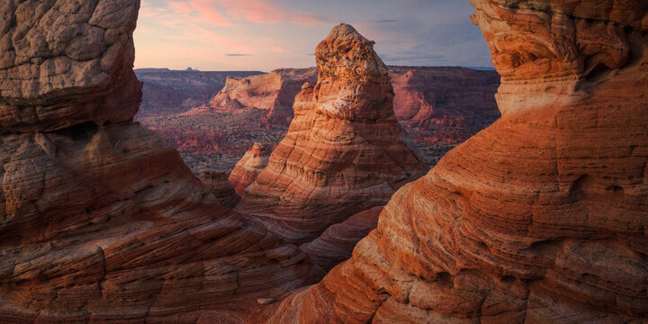 View of layered sandstone formations glow with warm light as the sun sets over a distant canyon landscape, Page, Arizona, United States.
