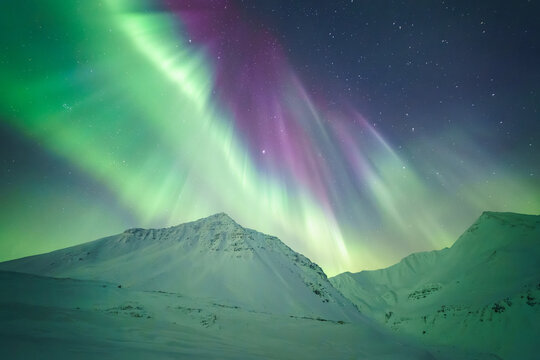 View of vibrant green and purple aurora borealis dancing above snow-capped mountains under a starry sky, a celestial ballet of light and color, Coldfoot, Alaska, United States.