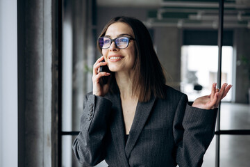 Fototapeta premium Business woman standing at the office window and talking on the mobile phone