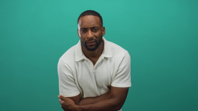 Man with crossed arms showing forearms and white polo shirt in teal studio three quarter closeup pose leaning slightly forward and facing camera; concern introspection.