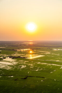 View of the golden sun sinking below the horizon, casting a warm glow on the green fields and shimmering water, Siem Reap, Siem Reap Province, Cambodia.