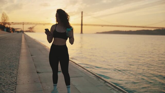 Sporty woman using smartphone after workout at sunset