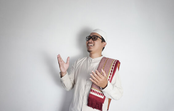 Asian Muslim man raises both hands forward, praying devoutly. A man in a koko shirt, white peci and a prayer mat on his shoulder